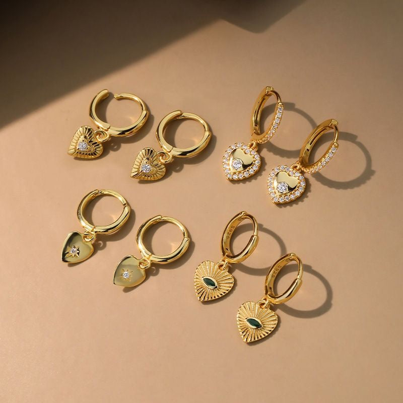 A pair of huggie earrings, one with a silver finish and the other with a gold vermeil finish, each featuring a small dangling design.