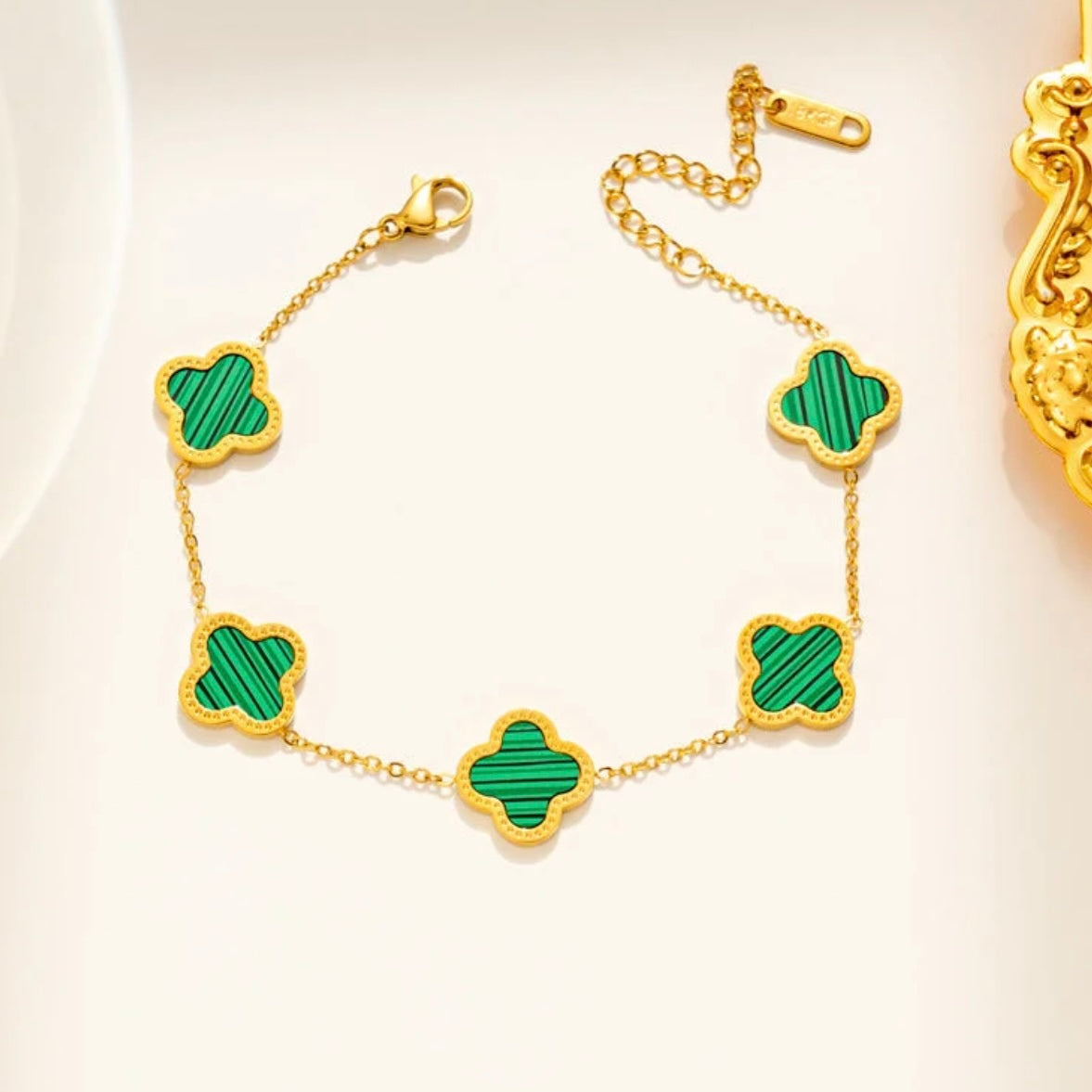 Gold bracelet with green clover-shaped charms on a white background