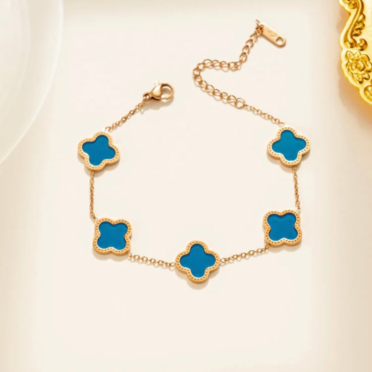 Gold bracelet with blue clover-shaped charms on a light background
