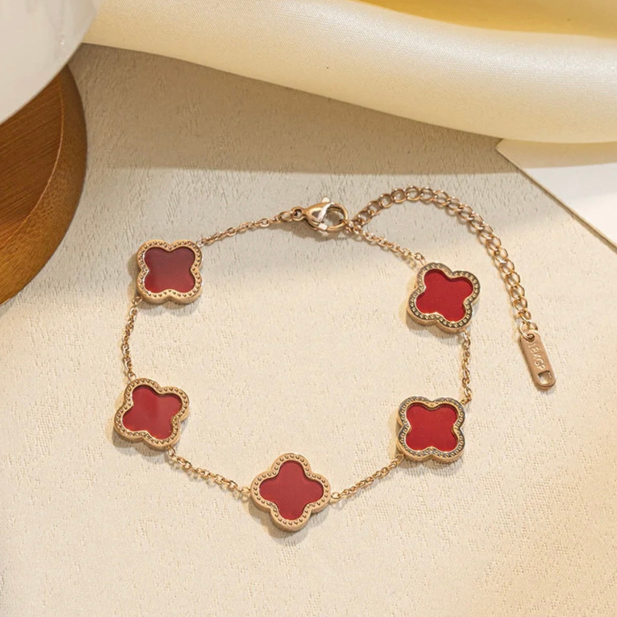 Gold bracelet with red clover-shaped charms on a light beige surface