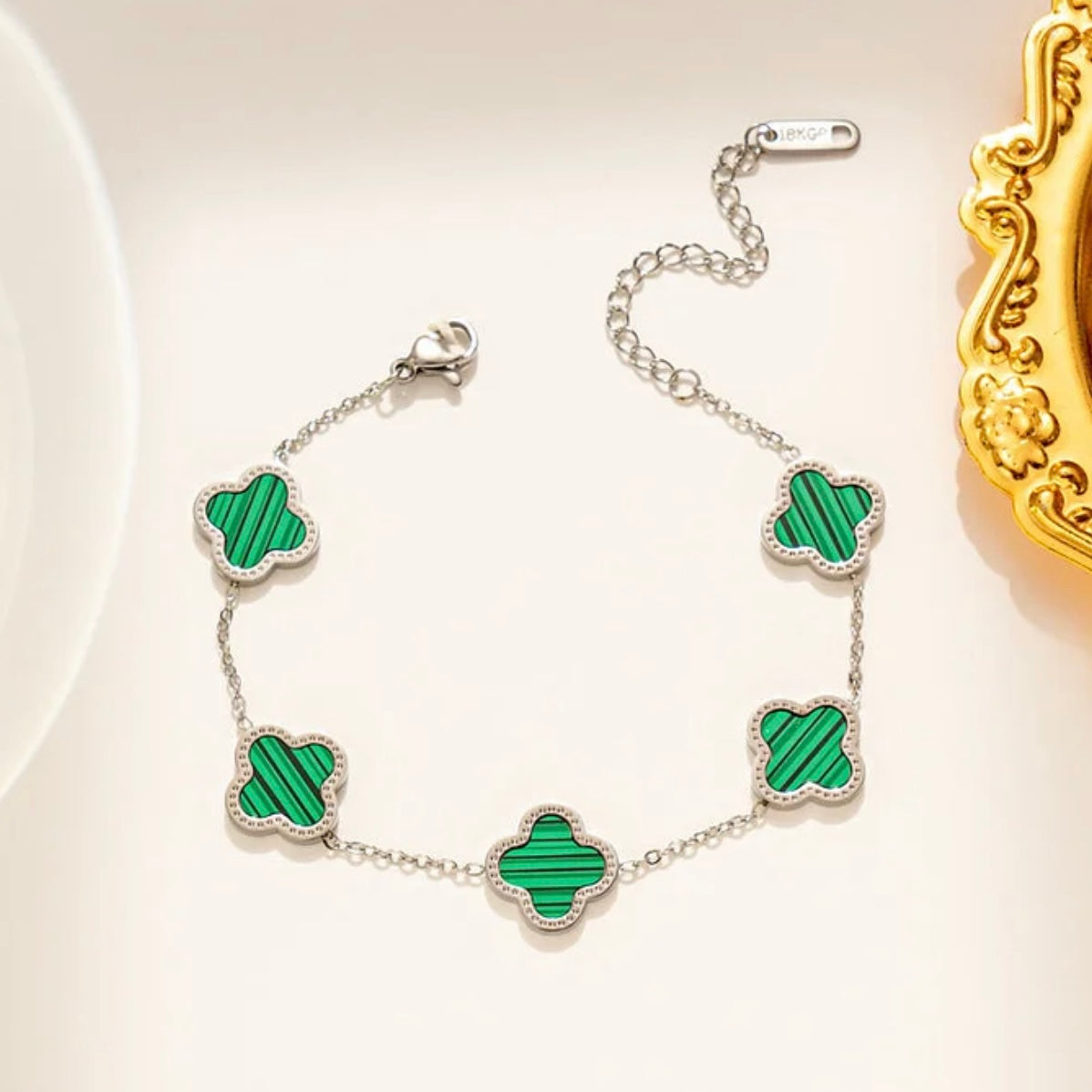 Silver bracelet with green clover-shaped charms on a light background