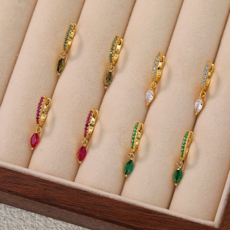 A pair of huggie earrings, one with a silver finish and the other with a gold vermeil finish, each featuring a small dangling design.