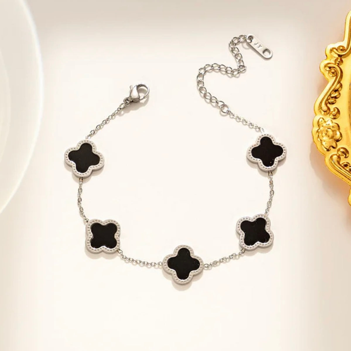 Silver bracelet with black clover-shaped charms on a light background