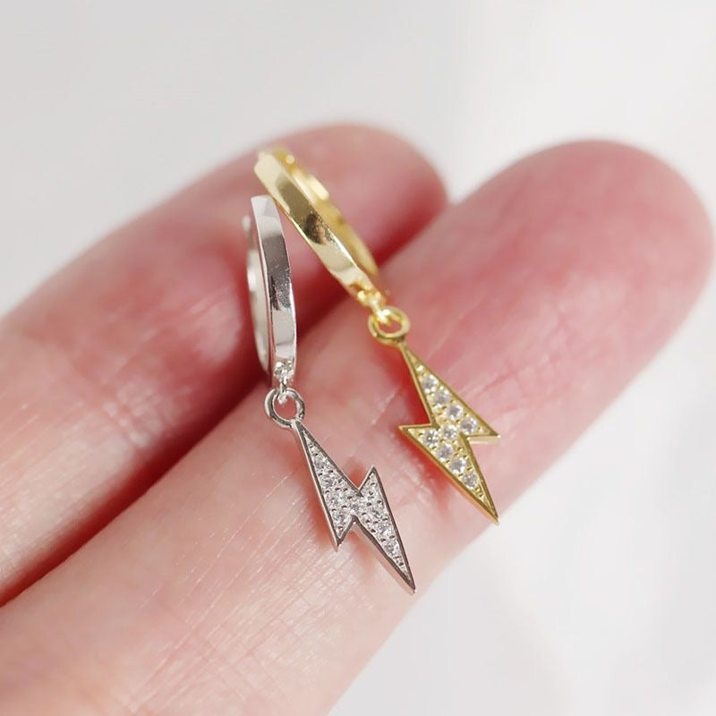 A pair of huggie earrings, one with a silver finish and the other with a gold vermeil finish, each featuring a small dangling design.