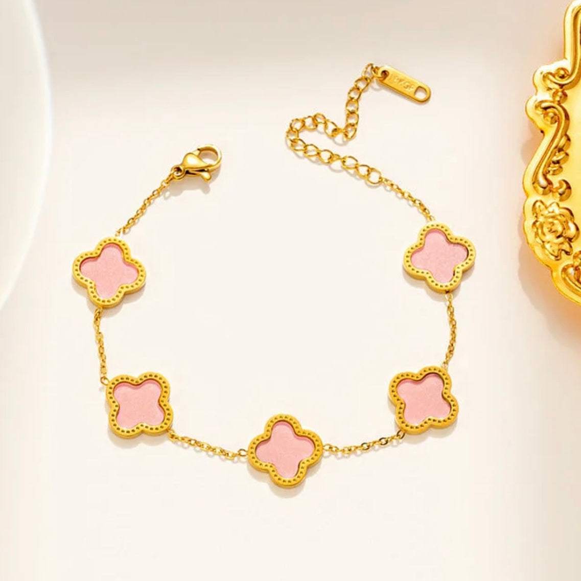Gold bracelet with pink clover-shaped charms on a light background