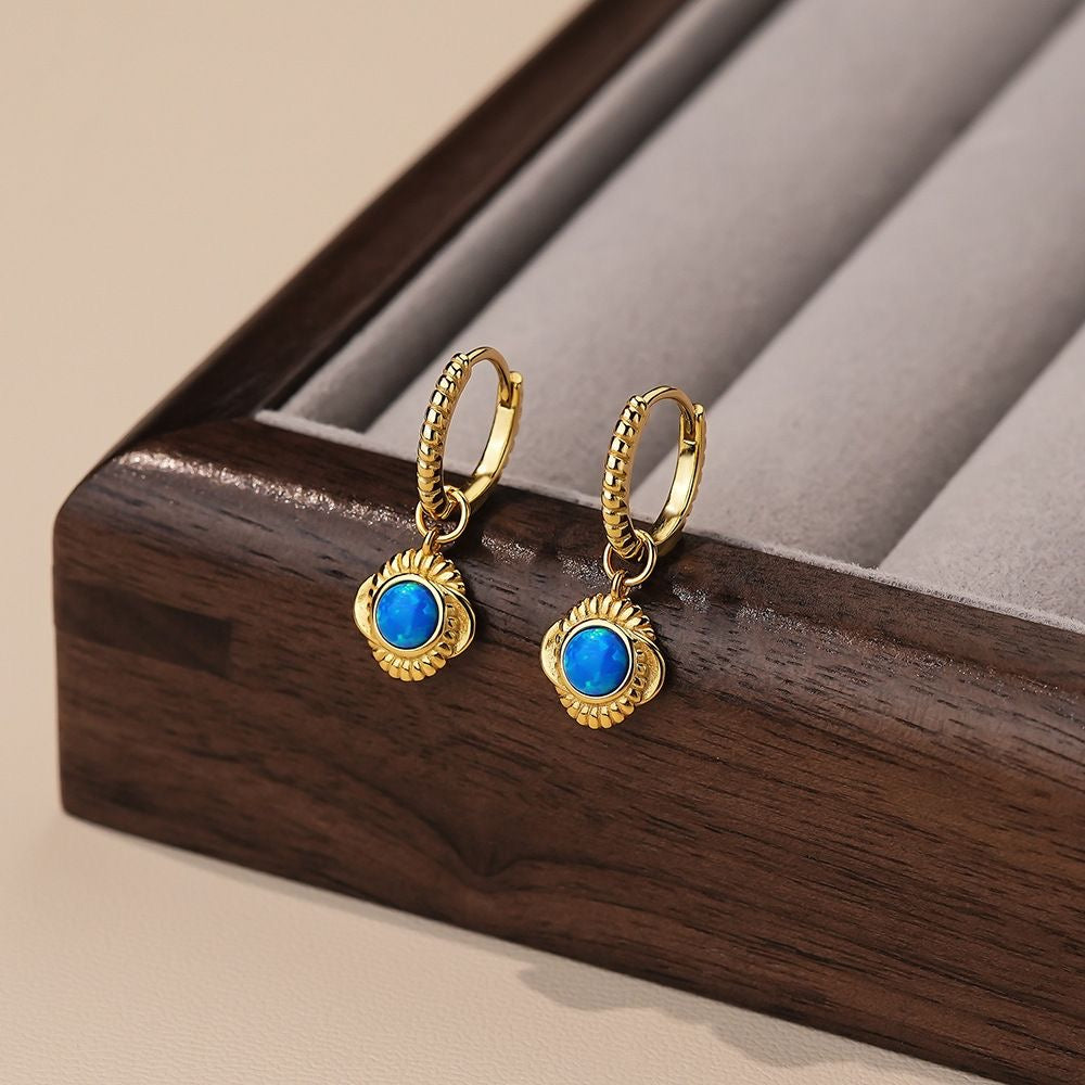 A pair of huggie earrings, one with a silver finish and the other with a gold vermeil finish, each featuring a small dangling design.