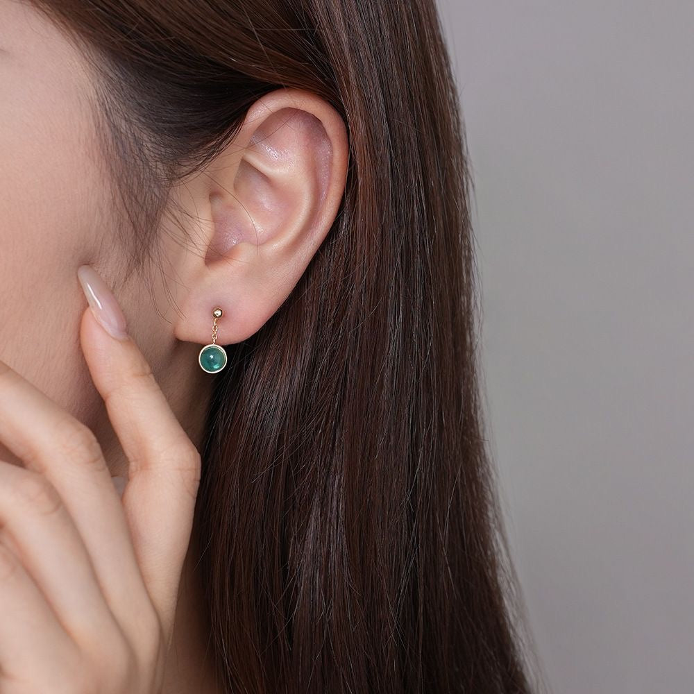 A pair of huggie earrings, one with a silver finish and the other with a gold vermeil finish, each featuring a small dangling design.