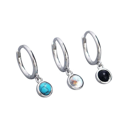 A pair of sterling silver hoop huggie earrings with a round stone drop charm in different color options.